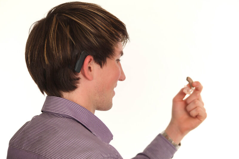 Signalhund für schwerhörigen Mann, der sein Hörgerät in der Hand hält